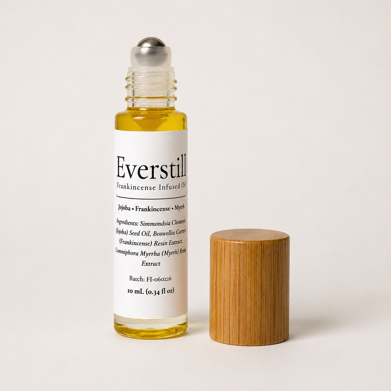 Everstill Frankincense & Myrrh resin-infused jojoba oil roll-on with stainless steel roller ball and bamboo cap beside bottle.